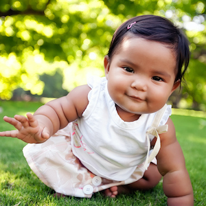 Cute baby girl with a smile on her face, reaching out to take her first crawling step on a lush green lawn at an outdoor park, of mixed ethnic race. (Cute baby girl with a smile on her face, reaching out to take her first crawling step on a lush green